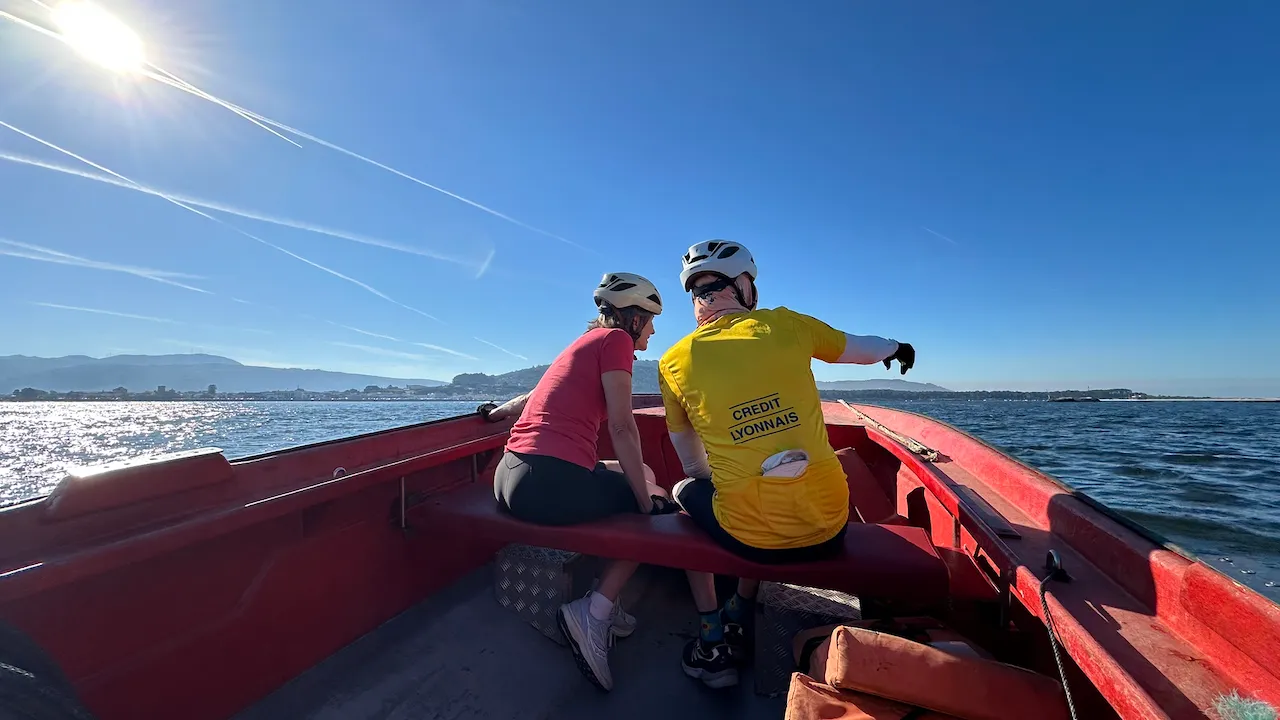 Two cyclists in helmets crossing the Minho in the bow of our red taxi boat.